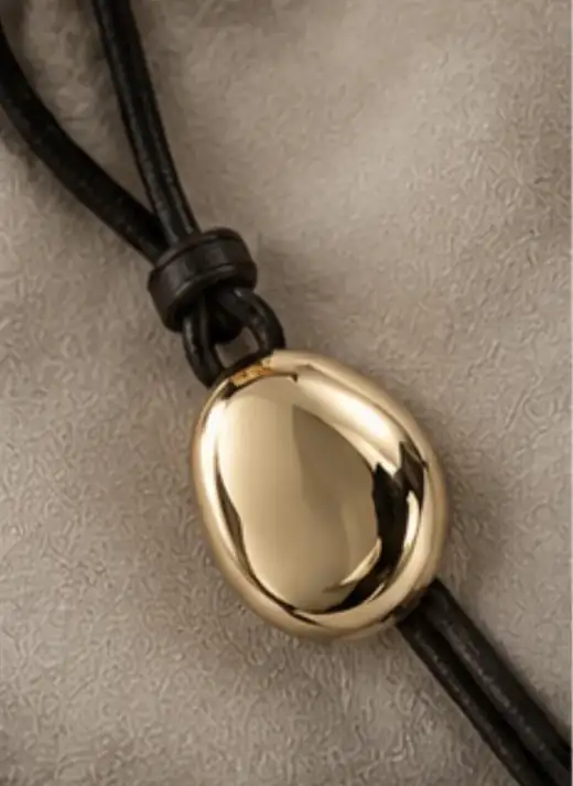 Goldener Anhänger in organischer Form an einem schwarzen Lederband